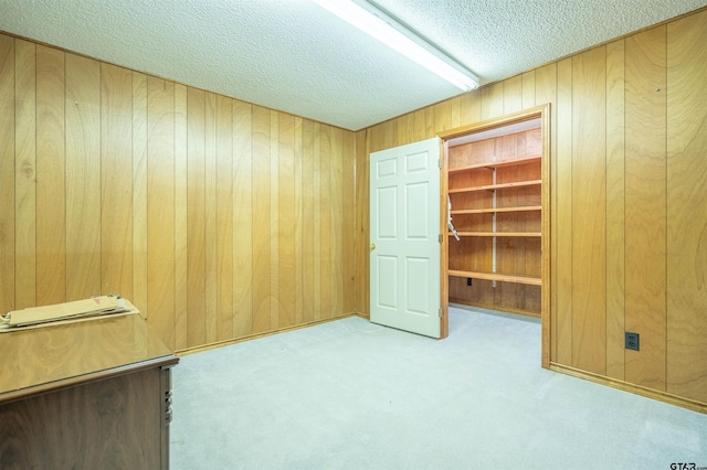 interior space with wood walls, a textured ceiling, and light carpet