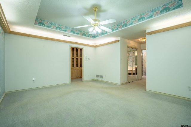 empty room featuring a textured ceiling, light carpet, ceiling fan, and a raised ceiling