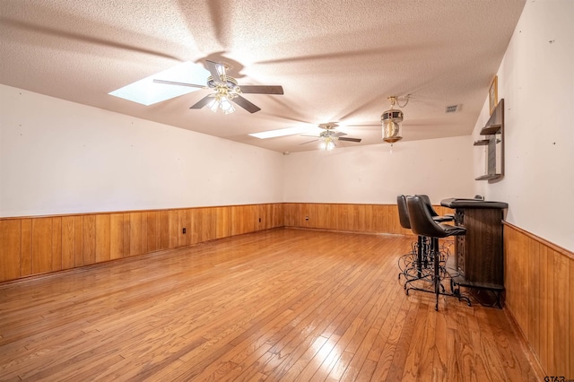 interior space featuring ceiling fan, a textured ceiling, bar, and light hardwood / wood-style flooring