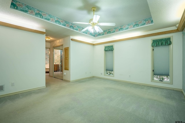 carpeted empty room featuring a textured ceiling, ceiling fan, and a tray ceiling