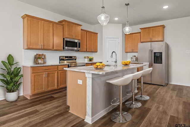 kitchen with dark hardwood / wood-style flooring, decorative light fixtures, a breakfast bar area, a kitchen island with sink, and appliances with stainless steel finishes