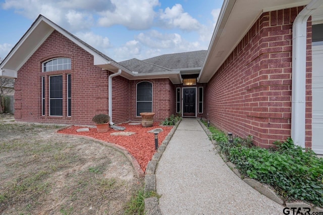 property entrance featuring a shingled roof and brick siding