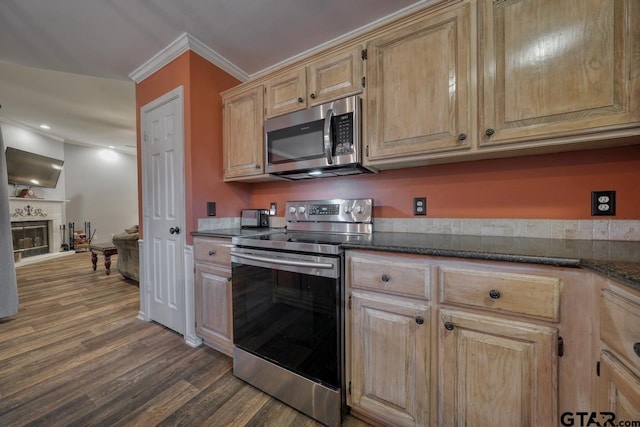 kitchen featuring dark wood-style floors, stainless steel appliances, ornamental molding, a glass covered fireplace, and light brown cabinets