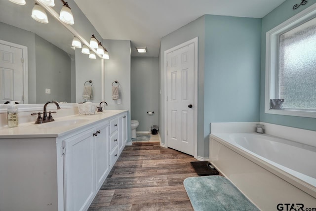 bathroom featuring toilet, wood finished floors, a sink, a bath, and double vanity