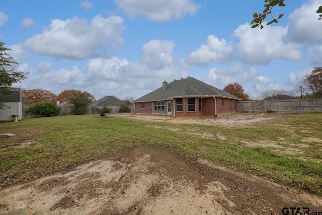 rear view of house featuring brick siding, a lawn, a chimney, and a fenced backyard