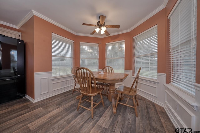 dining area featuring ceiling fan, ornamental molding, dark wood-type flooring, and wainscoting