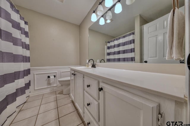 bathroom with toilet, a wainscoted wall, tile patterned floors, vanity, and a decorative wall