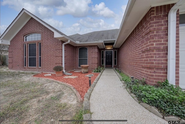 view of exterior entry featuring a shingled roof and brick siding