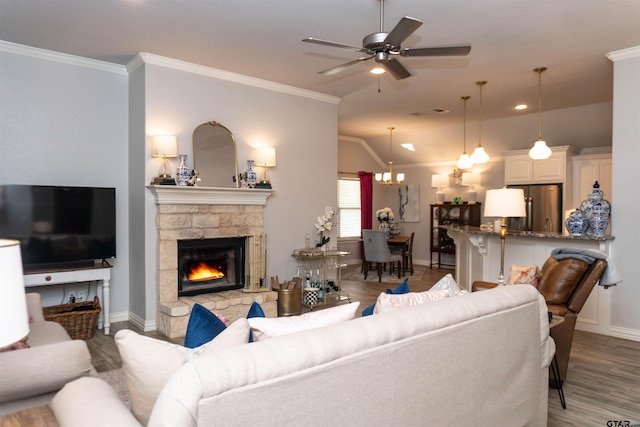 living room with dark hardwood / wood-style flooring, a stone fireplace, ceiling fan with notable chandelier, and crown molding