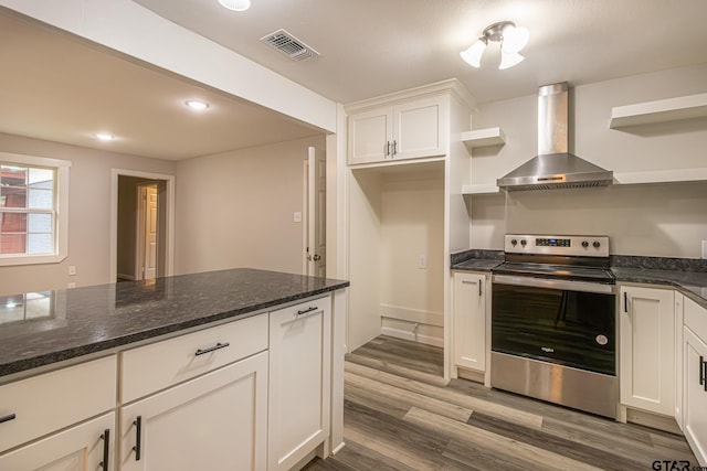 kitchen featuring stainless steel range with electric stovetop, dark stone counters, hardwood / wood-style floors, white cabinets, and wall chimney exhaust hood