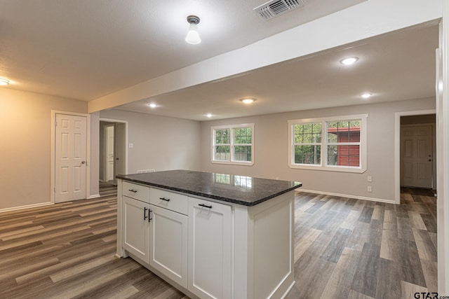 kitchen featuring dark wood-type flooring, a kitchen island, white cabinetry, and dark stone counters