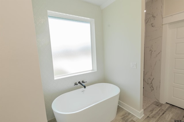 full bath featuring a freestanding bath, a wealth of natural light, wood finished floors, and baseboards