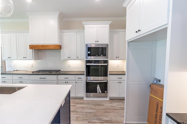 kitchen with white cabinets, stainless steel appliances, light wood-style floors, and dark stone counters
