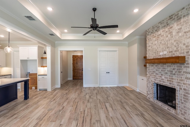 unfurnished living room with light wood finished floors, a tray ceiling, visible vents, a ceiling fan, and a fireplace