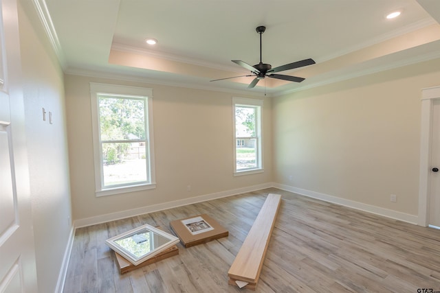 empty room featuring wood finished floors, ceiling fan, a raised ceiling, baseboards, and ornamental molding