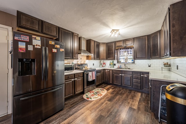 kitchen with sink, wall chimney range hood, dark hardwood / wood-style flooring, dark brown cabinets, and appliances with stainless steel finishes