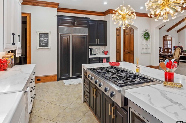 kitchen featuring ornamental molding, paneled built in refrigerator, light tile patterned floors, stovetop, and a chandelier