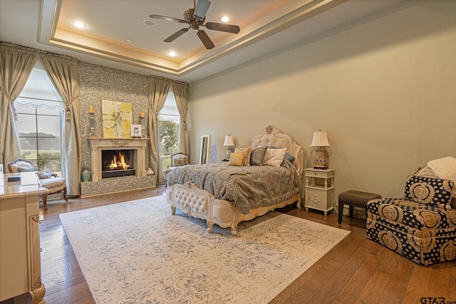 bedroom with a fireplace, ceiling fan, dark hardwood / wood-style floors, and a tray ceiling