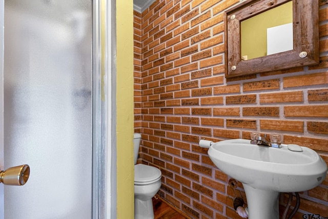 bathroom featuring brick wall and toilet
