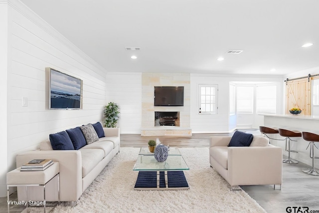 living room with crown molding, a barn door, a large fireplace, and light hardwood / wood-style flooring