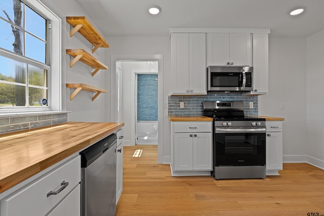 kitchen featuring butcher block counters, decorative backsplash, open shelves, and stainless steel appliances