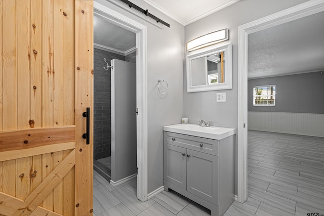 full bathroom featuring crown molding, a shower stall, a textured ceiling, vanity, and wainscoting