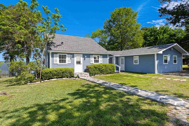 view of front of house featuring roof with shingles, fence, and a front lawn
