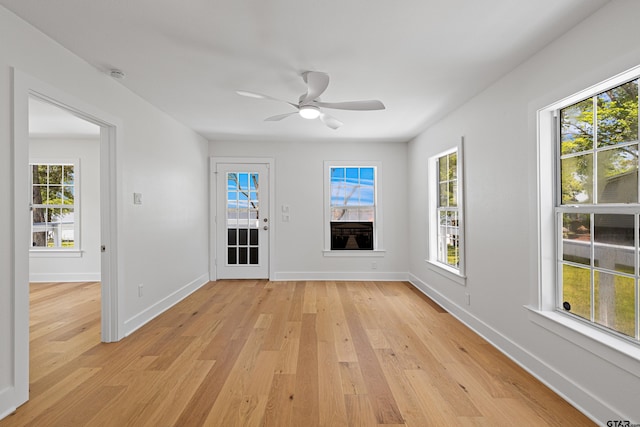 spare room with baseboards, light wood-type flooring, a ceiling fan, and a healthy amount of sunlight