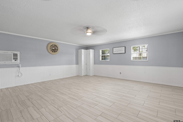 spare room with a textured ceiling, ornamental molding, a ceiling fan, and a wainscoted wall
