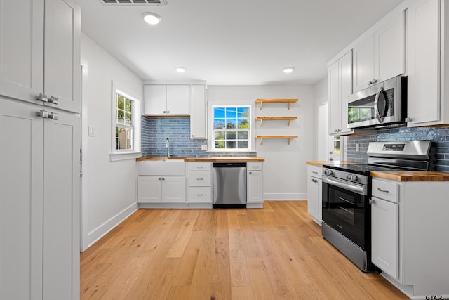 kitchen featuring butcher block counters, decorative backsplash, stainless steel appliances, light wood finished floors, and a sink