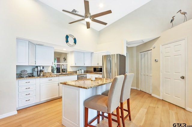 kitchen with a center island, sink, light stone countertops, white cabinetry, and stainless steel appliances