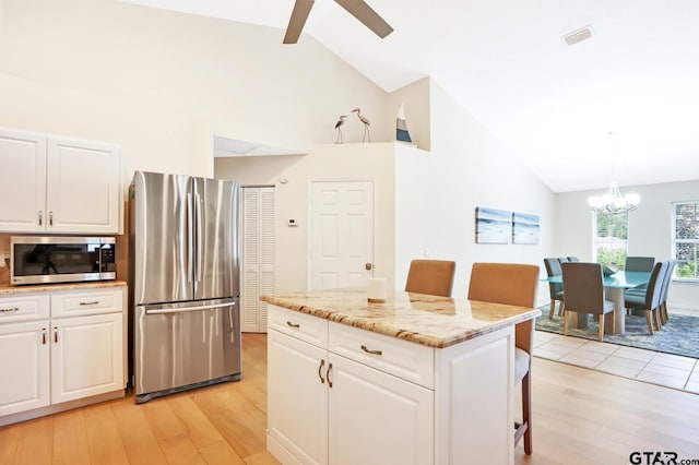 kitchen with pendant lighting, a center island, white cabinets, appliances with stainless steel finishes, and a kitchen bar