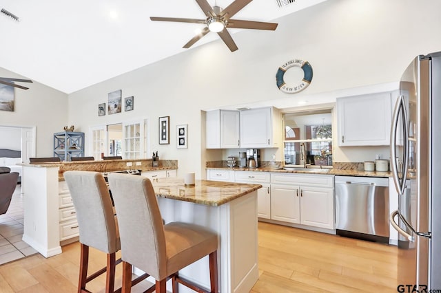 kitchen featuring appliances with stainless steel finishes, a kitchen breakfast bar, light stone counters, sink, and white cabinetry