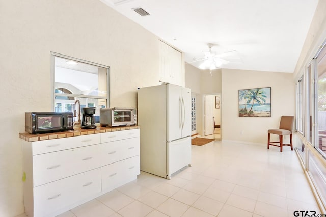 kitchen with ceiling fan, light tile patterned flooring, tile countertops, white fridge, and white cabinets