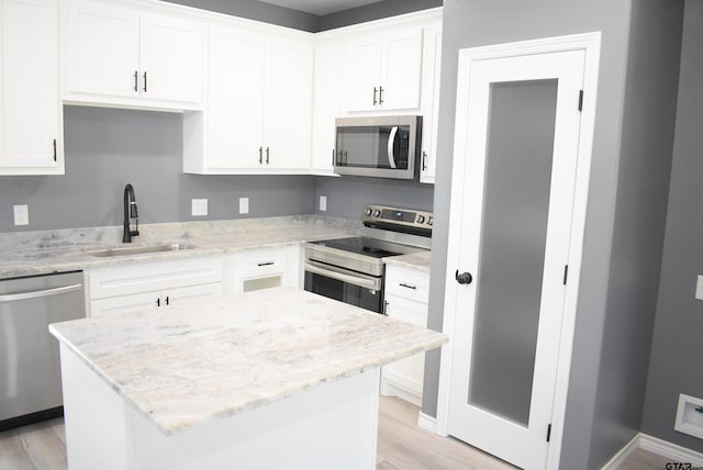 kitchen featuring a center island, sink, light stone counters, white cabinetry, and stainless steel appliances