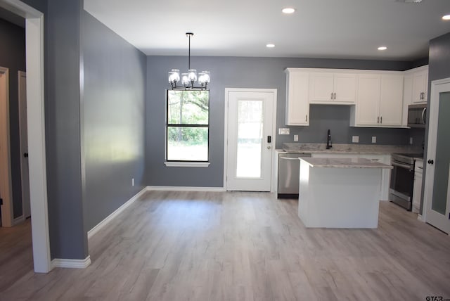 kitchen with stainless steel appliances, white cabinets, a notable chandelier, light hardwood / wood-style floors, and a kitchen island