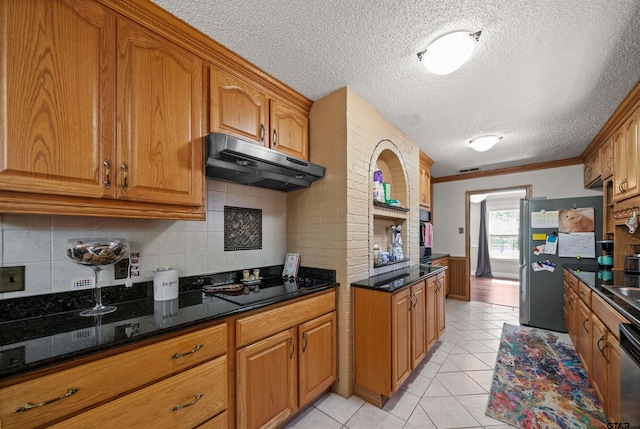 8312 Oxford Dr, Tyler, TX 75703 - kitchen featuring under cabinet range hood, appliances with stainless steel finishes, brown cabinetry, a textured ceiling, and decorative backsplash