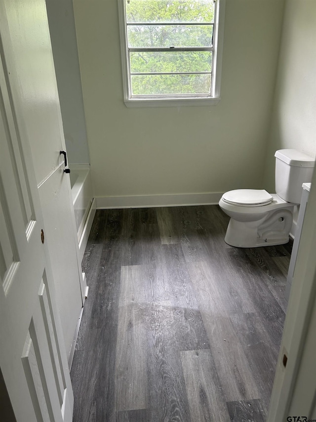 bathroom with baseboards, a tub to relax in, toilet, and wood finished floors