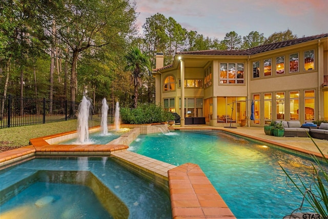 pool at dusk featuring an in ground hot tub, outdoor lounge area, and pool water feature