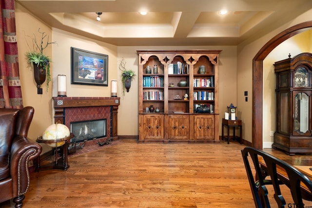 living area with a tray ceiling, a tile fireplace, and light wood-type flooring