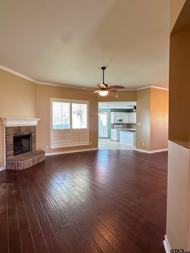 unfurnished living room with crown molding, ceiling fan, dark hardwood / wood-style flooring, and a brick fireplace