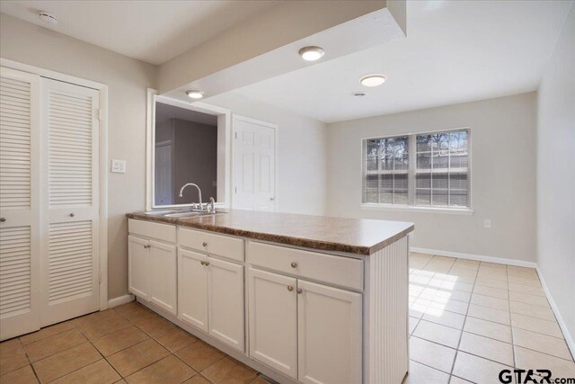 kitchen with light tile patterned floors, baseboards, a peninsula, a sink, and white cabinetry