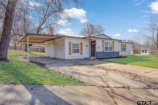 view of front facade with fence, a front yard, a chimney, a carport, and driveway