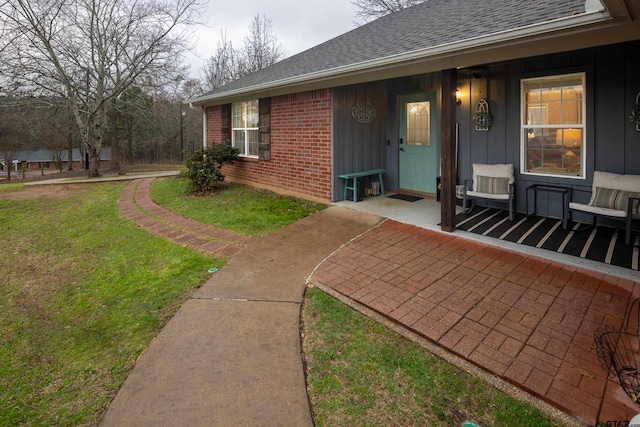 doorway to property with a shingled roof, brick siding, a lawn, and board and batten siding