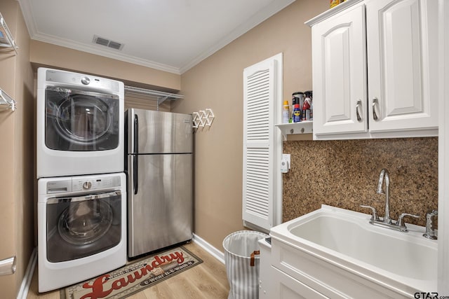 laundry room with cabinets, sink, crown molding, stacked washer and dryer, and light hardwood / wood-style flooring