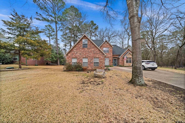 traditional-style home with driveway, roof with shingles, a front lawn, and brick siding