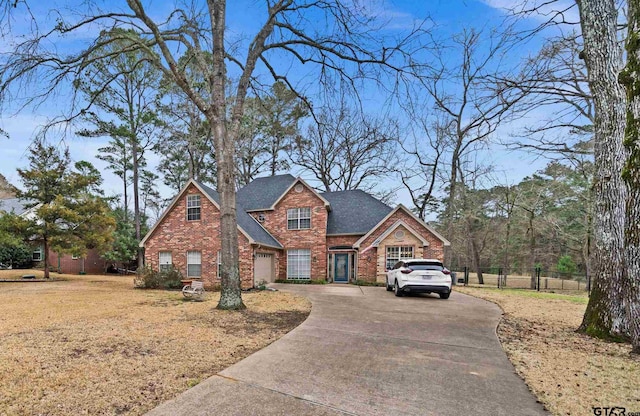 view of front facade with concrete driveway, brick siding, a shingled roof, and fence