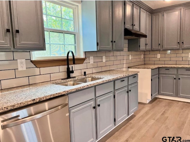 kitchen featuring tasteful backsplash, light stone counters, stainless steel dishwasher, sink, and light hardwood / wood-style flooring