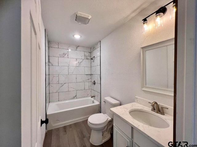 full bathroom with vanity, hardwood / wood-style flooring, tiled shower / bath combo, toilet, and a textured ceiling