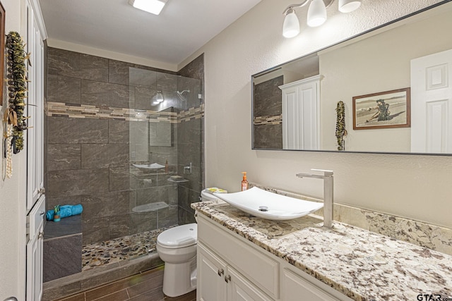 bathroom featuring toilet, vanity, hardwood / wood-style floors, and tiled shower